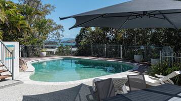 Piscina amb vora corba, envoltada per una tanca i zona de seients coberta amb taula i cadires.