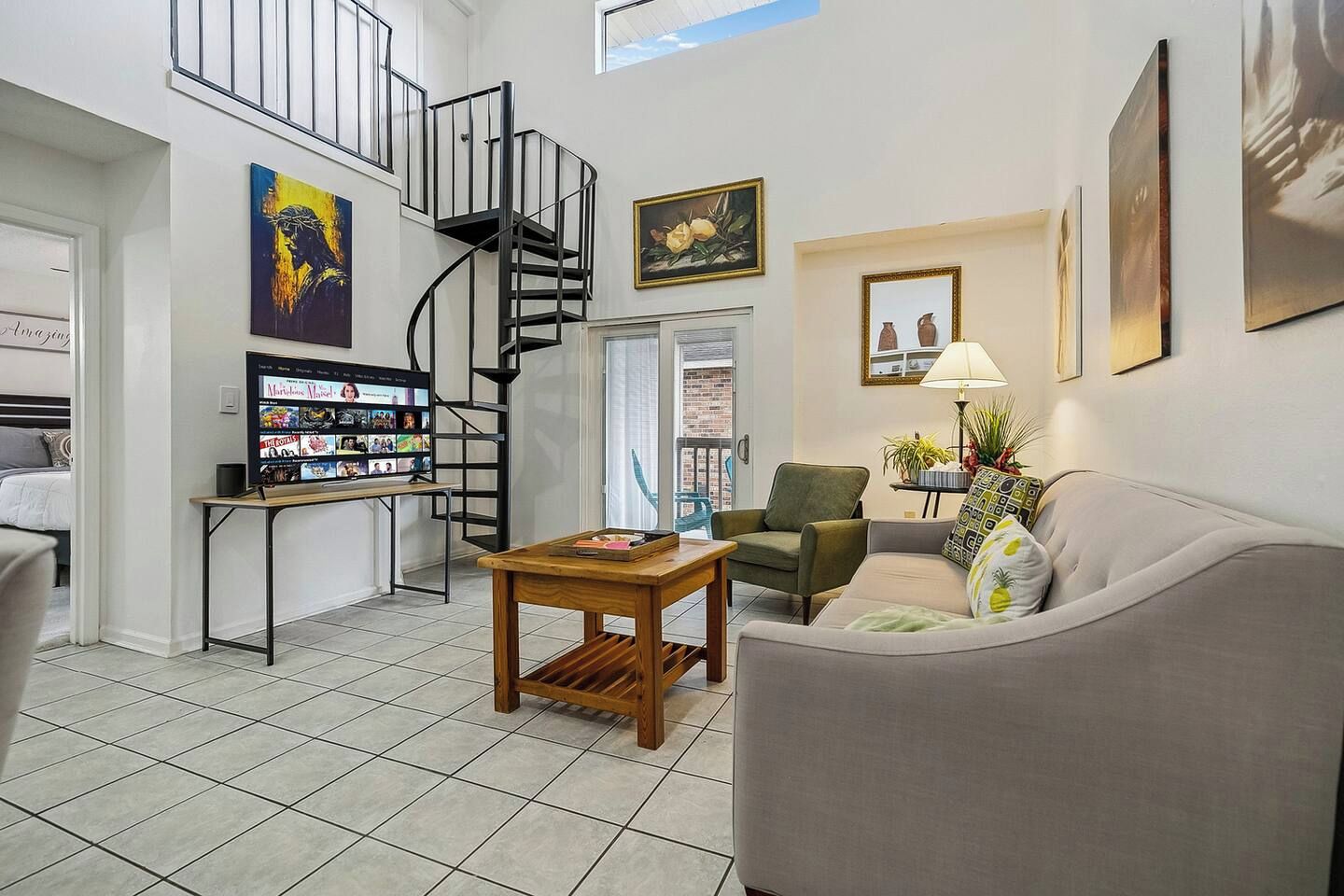 A living room with a sofa, a small table, a TV, a spiral staircase, and a balcony.