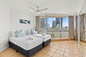 A hotel room with two beds, a ceiling fan, a city view, and a balcony with curtains. - Focus Apartments 2 Bedroom Ocean View (Surfers Paradise)