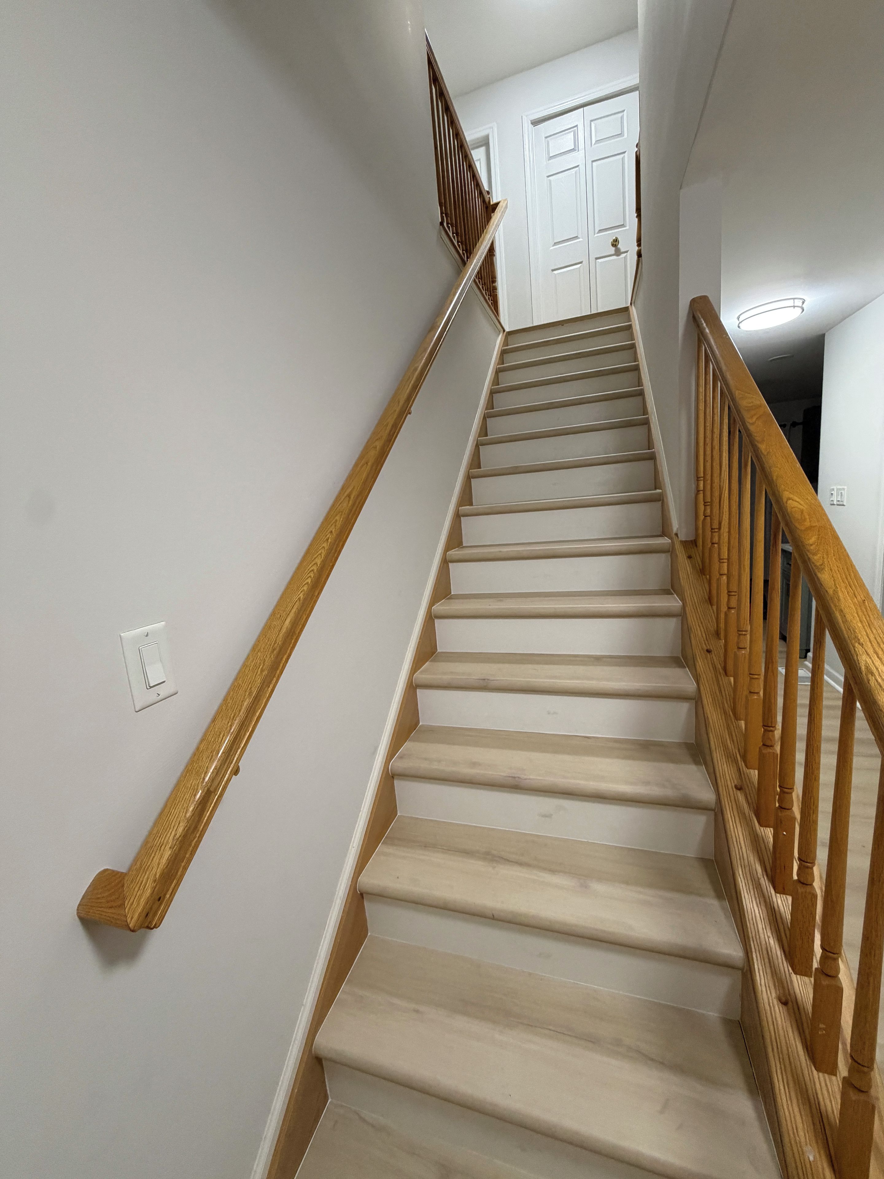 A staircase with wooden handrails and beige steps leading to a white door at the top.