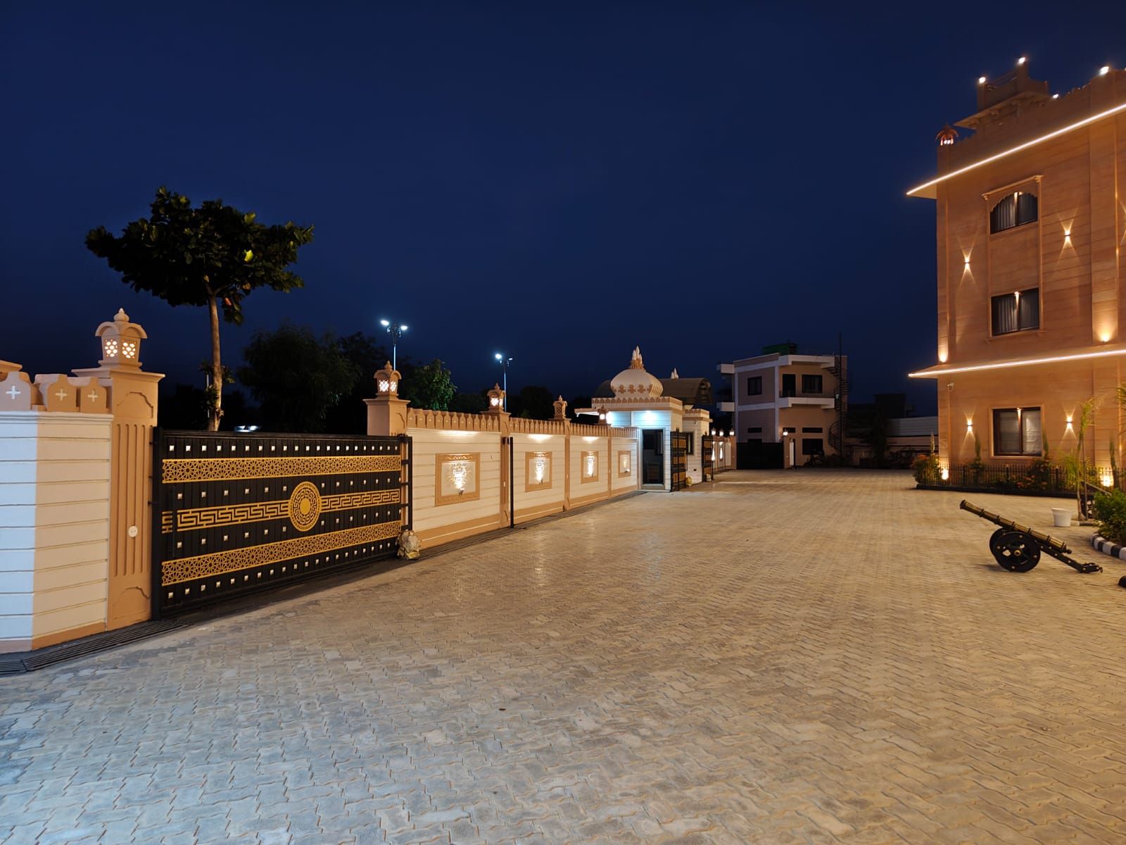 A paved courtyard with a decorative gate, a building entrance, and a parked vehicle.