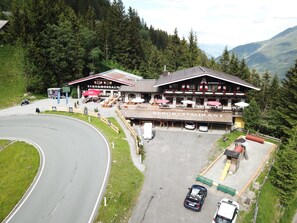 Restaurante com área externa, estacionamento e montanhas ao fundo.
