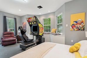 A bedroom with a bed, a gaming chair, a gaming console, and a window with a view of trees. - 5BR All King Beds Nature Mansion Retreat (Covington)
