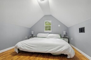 A bedroom with a sloped ceiling, a single bed, two bedside tables with lamps, a window with a view of greenery, and a wall-mounted air vent. - 5BR All King Beds Nature Mansion Retreat (Covington)