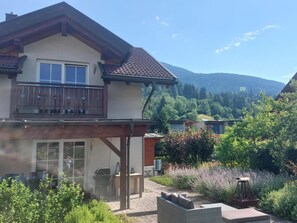 A two-story house with a balcony, a patio area with outdoor furniture, and a mountainous backdrop. - Vacation home with a large south-facing garden (Kötschach-Mauthen)
