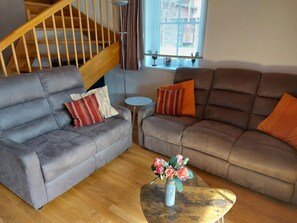 A living room with two sofas, a small table with a vase, a staircase, and a window with blinds. - Vacation home with a large south-facing garden (Kötschach-Mauthen)