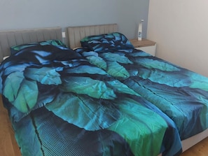 Een bed met een gestreept bedovertrek, een nachtkastje met een lamp en een wandklok.