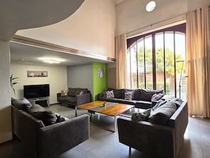 A modern living room with a flat-screen TV, two sofas, a coffee table, and a large window with curtains. - Cottage with indoor pool & sauna (costs incl.) (Waimes)