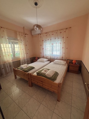 A room with two wooden beds, a ceiling fan, and a window with curtains. - Pancho Villa Family Apartments (Kallithea Pieras)