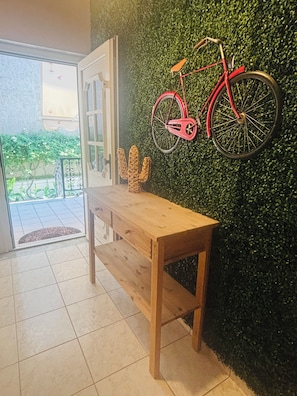 A wooden bench in a room with a green wall, a red bicycle, and a cactus decoration. - Pancho Villa Family Apartments (Kallithea Pieras)