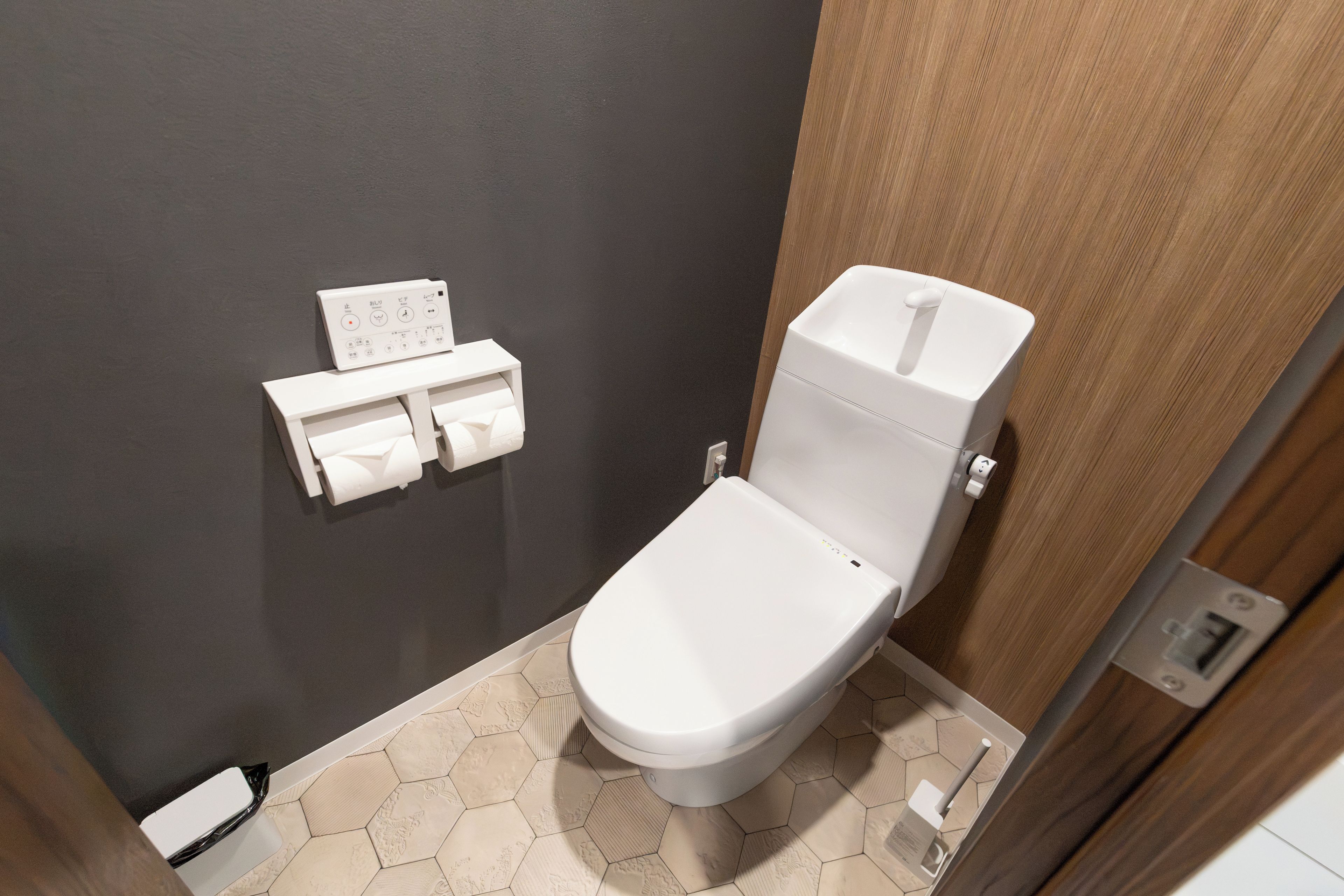 Um banheiro pequeno com vaso sanitário branco, porta-papel higiênico e piso com padrão hexagonal.