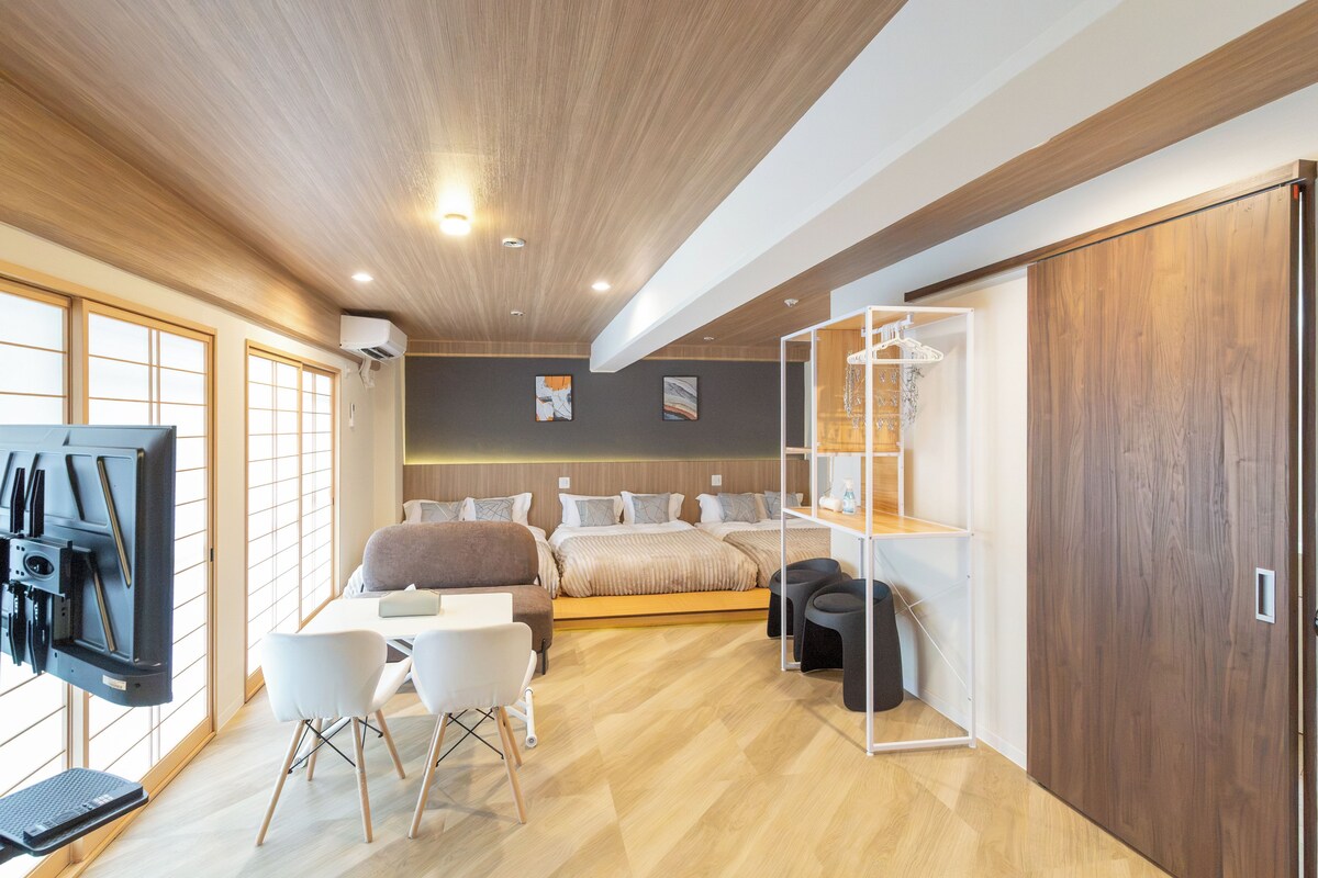 A modern hotel room with a bed, a desk, chairs, a TV, and a wardrobe.