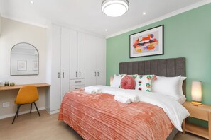 Ein Hotelzimmer mit einem Bett, einem Schreibtisch und einem Stuhl. An der Wand hängt ein Gemälde, und auf dem Nachttisch steht eine Lampe.