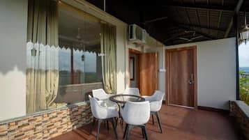 Uma varanda com uma mesa redonda e cadeiras, uma porta de madeira e vista para a paisagem.
