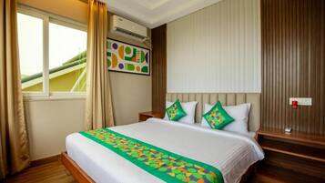 Quarto de hotel com cama, janela, cortinas, ar condicionado, obra de arte na parede e mesa de cabeceira com abajur.