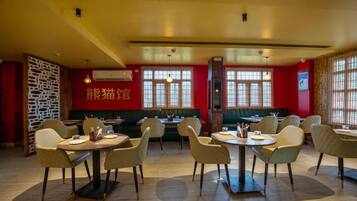 Interior de restaurante com mesas redondas, cadeiras e parede vermelha com caracteres chineses.