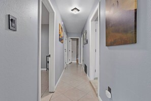 Un couloir aux murs blancs, doté d’un sol carrelé et de portes donnant sur d’autres pièces.
