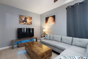 A modern living room with a flat-screen TV, a wooden coffee table, a grey sofa, and two wall-mounted paintings. - Bible Themed Gulf Beach Escape (Gulfport)