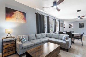 A modern living room with a sectional sofa, a wooden coffee table, a side table with a lamp, and a dining area with a table and chairs. - Bible Themed Gulf Beach Escape (Gulfport)