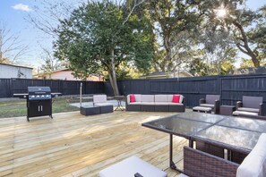 Une terrasse extérieure équipée d’un barbecue, d’un espace salon et d’une table à plateau en verre.