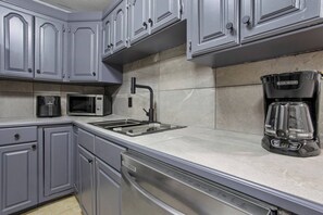 A modern kitchen with grey cabinets, a stainless steel sink, a black coffee maker, and a microwave. - Bible Themed Gulf Beach Escape (Gulfport)