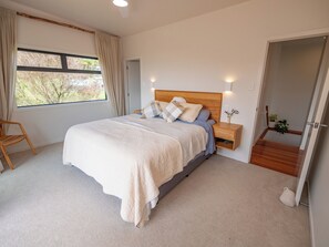 Ein Schlafzimmer mit einem Bett, Nachttischen, einem fenster mit Vorhängen, einer Tür und einer Treppe.