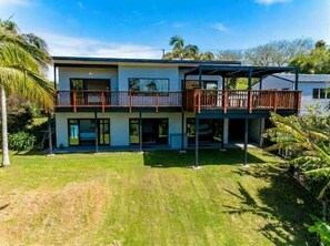 Ein zweigeschossiges Haus mit einem Balkon im oberen Geschoss, umgeben von einem gepflegten Rasen und Palmen.