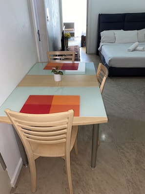 A modern living room with a glass-top dining table, two wooden chairs, a sofa, and a bed with white bedding. - kualalumpur Bukit Bintang Fairlane Residence Rooftop Swimming Pool (Kuala Lumpur)