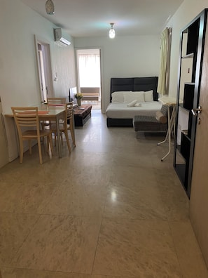 Habitación de hotel con cama, escritorio y silla. Se observa una ventana con cortinas, un ventilador de techo y una puerta.