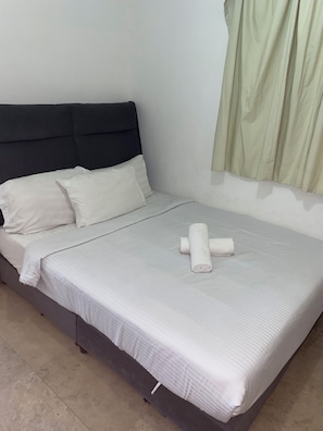 A neatly made bed with white linens and a rolled towel, a dark headboard, and a plain wall with a curtain. - kualalumpur Bukit Bintang Fairlane Residence Rooftop Swimming Pool (Kuala Lumpur)