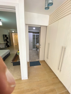 A hallway leading to a bathroom with a shower and toilet, a bed with a mattress and pillows, and a small table with a vase. - kualalumpur Bukit Bintang Fairlane Residence Rooftop Swimming Pool (Kuala Lumpur)