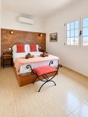 Ein Schlafzimmer mit Backsteinwand, einem Bett mit rosa Bettdecke, einer Bank und einem Fenster mit Blick.