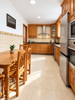 Eine Küche mit Holzschränken, einem Edelstahlkühlschrank und einer gefliesten Spritzschutzwand.