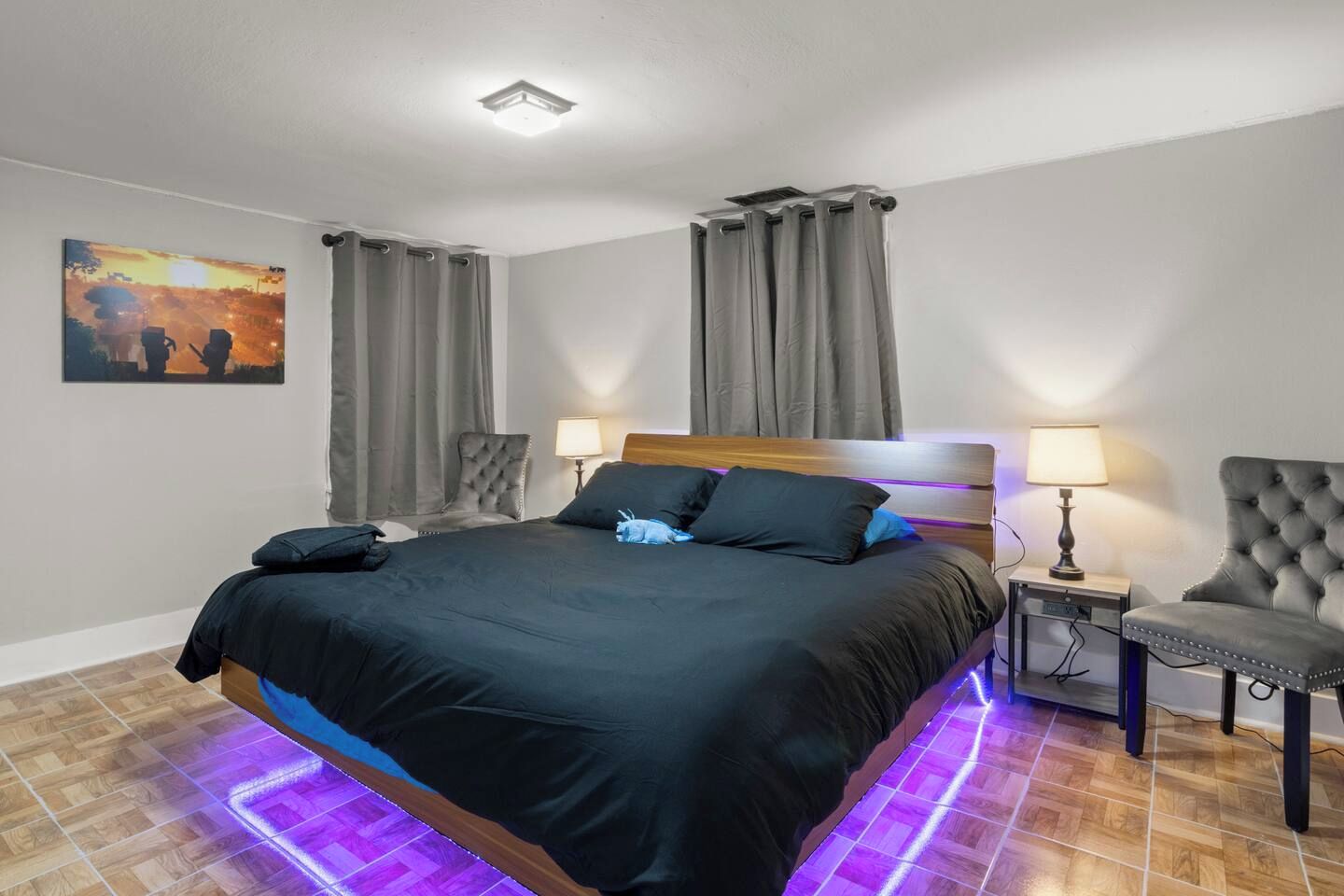 A hotel room with a bed, two bedside lamps, a chair, a painting, and a ceiling light.