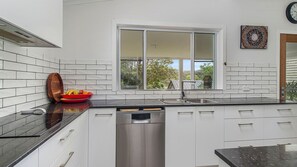 A modern kitchen with white cabinetry, a black countertop, and a window overlooking greenery. - Grant Street Getaway (Port Macquarie)