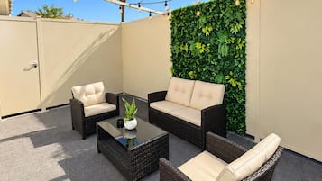 Pátio externo com móveis de vime, parede verde e luzes de corda.