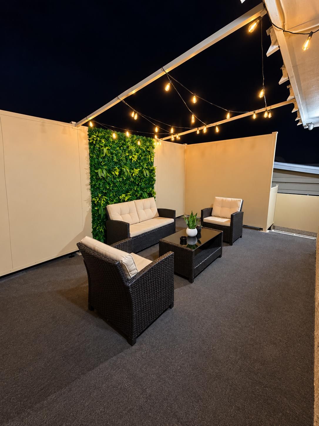 Um terraço no telhado com mobiliário de exterior, luzes de Natal e uma parede verde.
