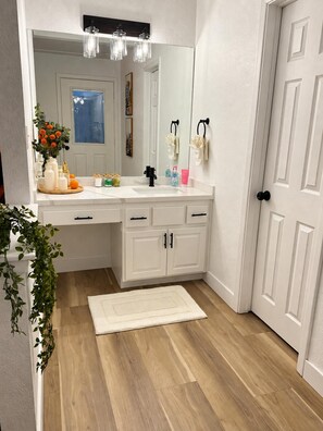 Une salle de bain avec un meuble-lavabo blanc, un miroir, un évier et une porte.