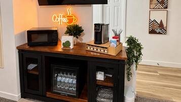 Ett vardagsrum med en platt-TV som är monterad på väggen, en neonreklamskylt med kaffetema, en mikrovågsugn, en kaffebryggare och ett skåp med förvaringsutrymme.