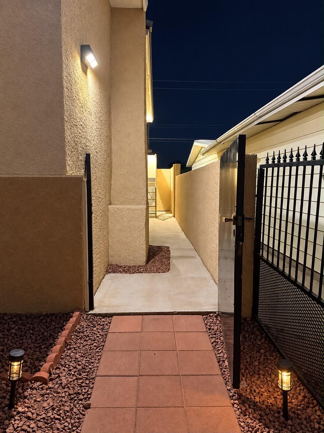 A gated pathway leading to a building at night with exterior lighting.