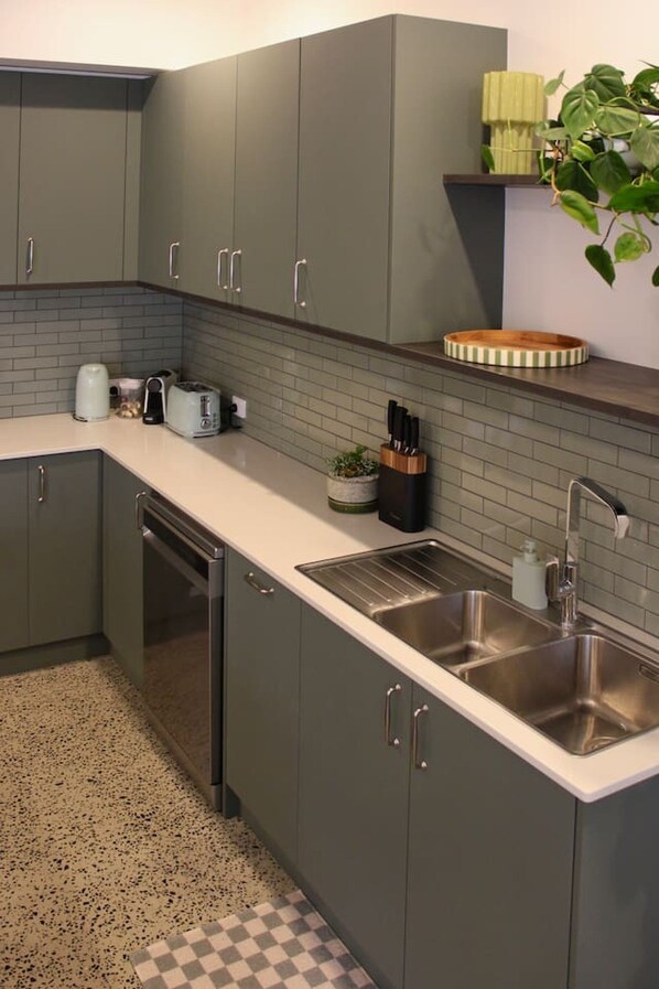 Een keuken met grijze kastjes, een roestvrijstalen spoelbak en een zwart-wit geruite vloer.
