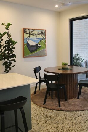 A dining area with a round table, four chairs, a potted plant, and a painting on the wall.