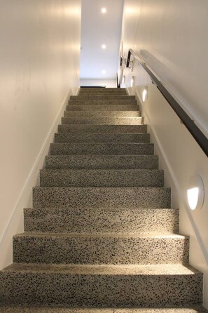 A staircase with a speckled floor, white walls, and wall-mounted lighting.