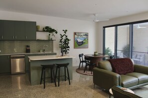 Eine moderne Küche mit einer zentralen Kochinsel, Barhocker, einem Essbereich mit Tisch und Stühlen sowie einem grünen Sofa.