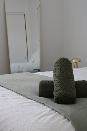 Een bed met een wit gewatteerde deken, een grijze plaid en twee opgerolde grijze dekens.