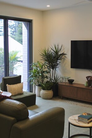 A modern living room with a sofa, a coffee table, a television, and a large window.