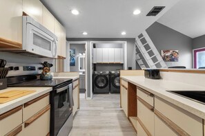 A modern kitchen with a microwave, oven, and sink, leading to a laundry area with washing machines. - X Men Themed King Bed with Bidet (Gulfport)