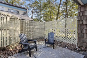 Eine Außenpatio-Terrasse mit zwei Adirondack-Stühlen, einem Holzzaun und einem Gebäude im Hintergrund.