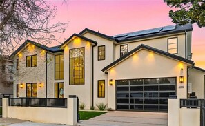 Une maison moderne à deux étages, dotée d’un garage, de grandes fenêtres et d’un éclairage extérieur soigné.