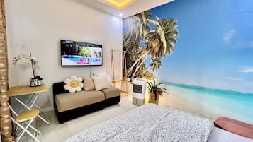 Ein Schlafzimmer mit einem Bett, einem Sofa, einem Fernseher und einem Wandbild einer Strandansicht.